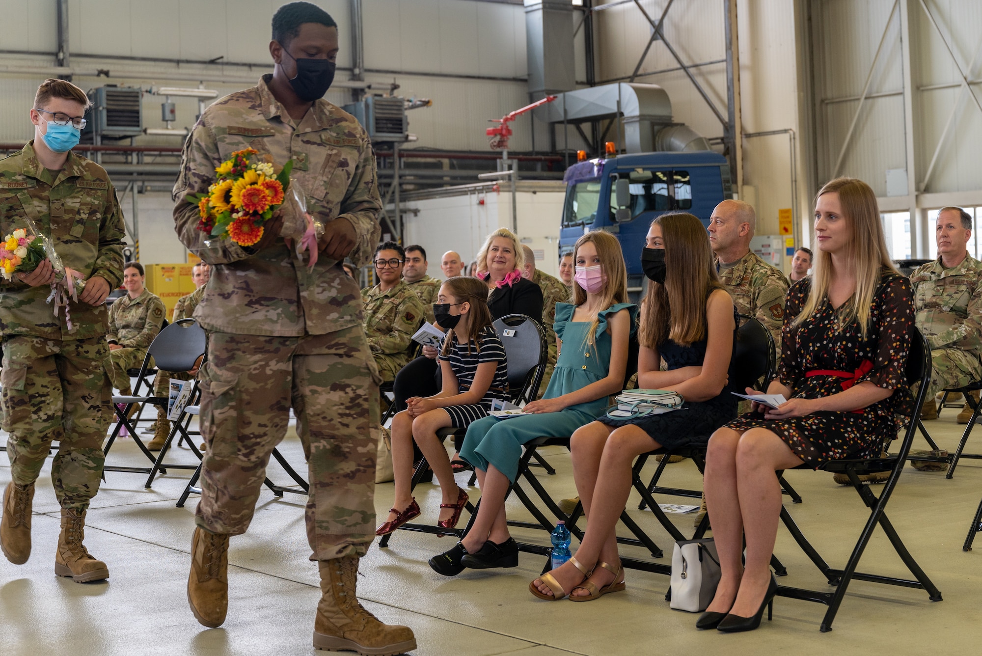 Airmen holding flowers and walking alongside seated crowd.