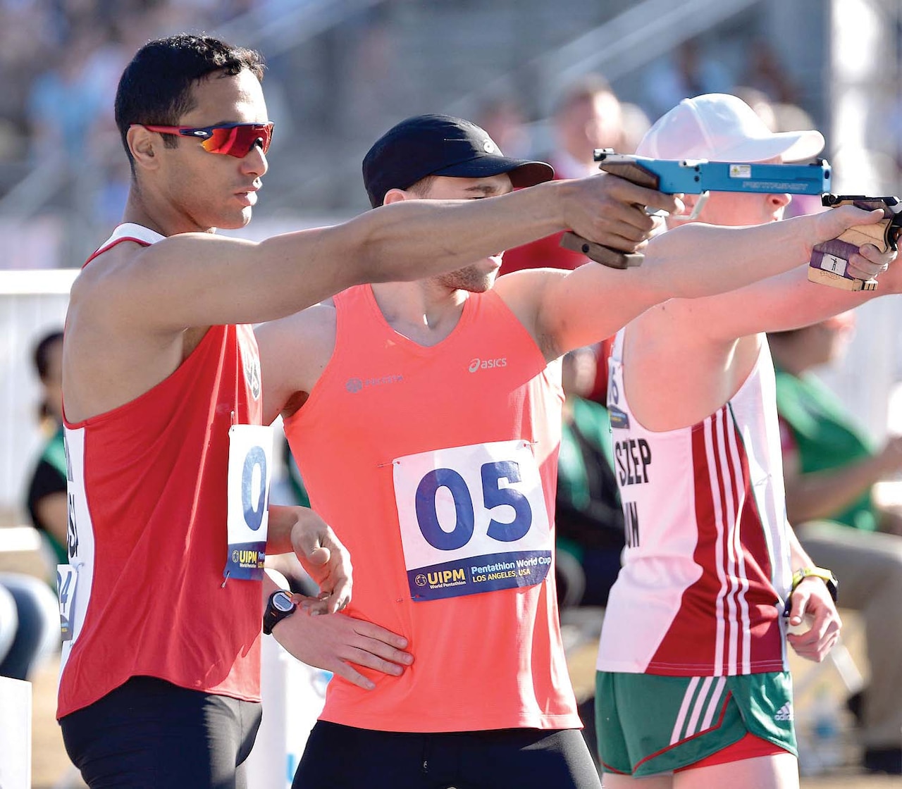 Men in athletic gear shoot guns during a pentathlon competition.