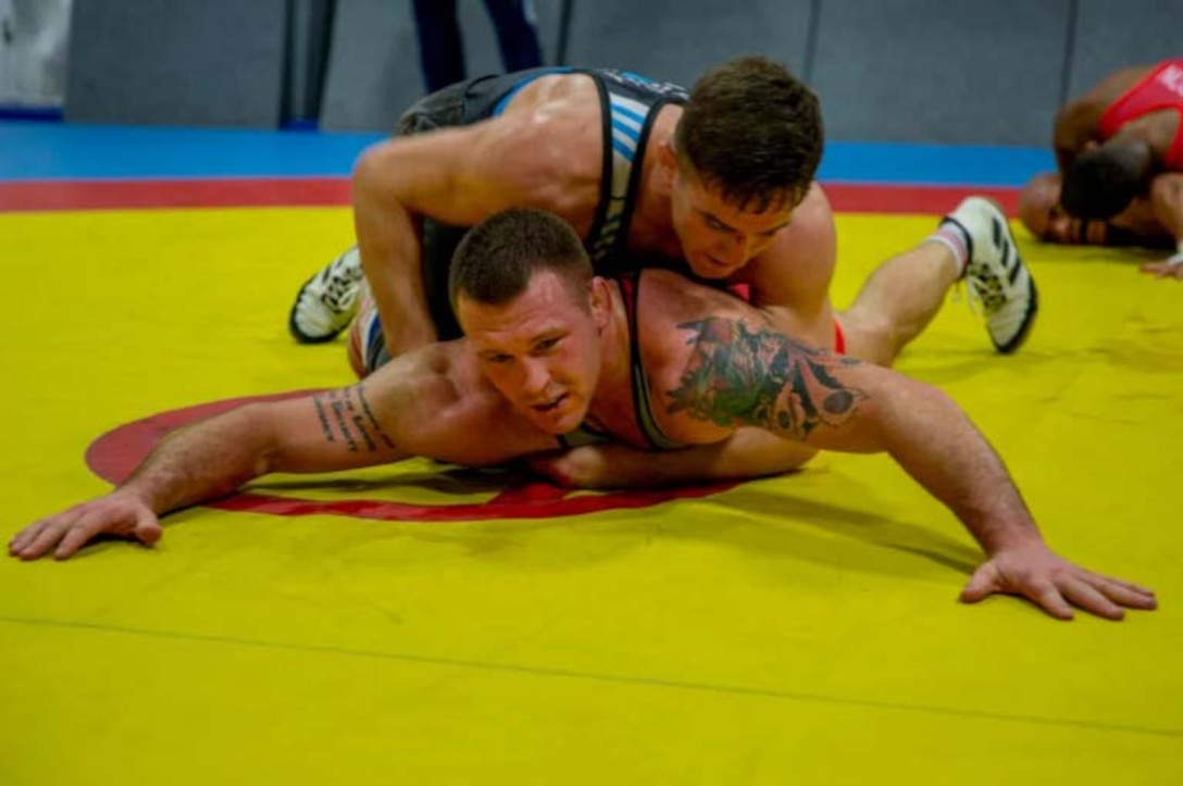 Two men practice wrestling skills on a yellow mat.