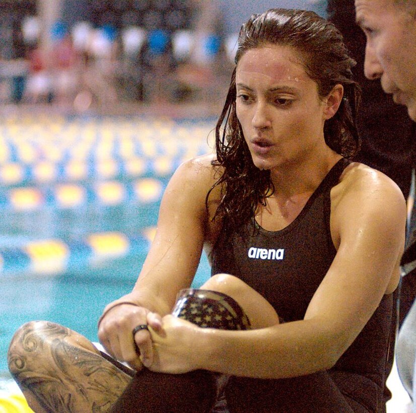 A female swimming athlete sits next to a pool.