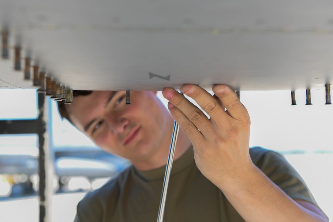 An aircraft electrical and environmental systems specialist assigned to the 555th Aircraft Maintenance Unit loosens screws on a U.S. Air Force F-16 Fighting Falcon at Graf Ignatievo Air Base, Bulgaria, July 9, 2021. Eight F-16s assigned to the 555th Fighter Squadron are participating in exercise Thracian Star 21, a multilateral training exercise with the Bulgarian air force, aimed to enhance the ability to rapidly deploy to remote locations and provide a credible force to assure stability for the region. (U.S. Air Force photo by Airman 1st Class Brooke Moeder)