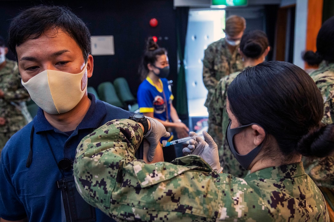 A sailor wearing a face mask gives a man wearing a face mask the COVID-19 vaccine.