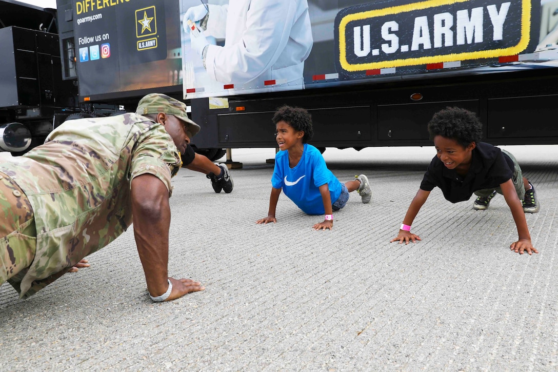 A soldier does pushups with two children.