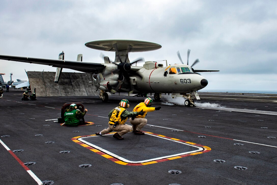 Sailors direct an aircraft as it launches from a ship’s deck.