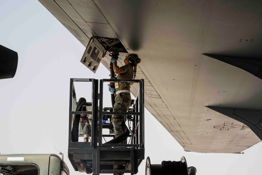 An airman stands on an elevated platform and loads cargo into an aircraft.