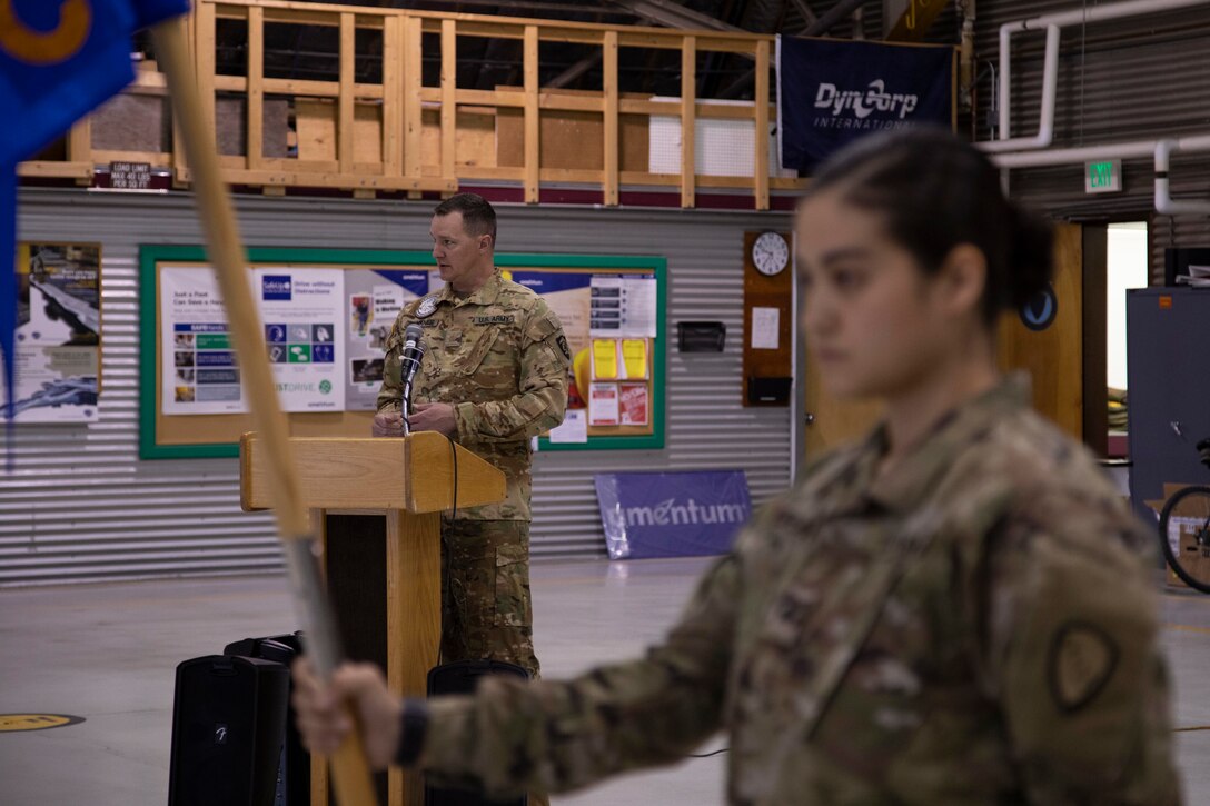 Sgt. Annalisa Copeland holds the company colors while Maj. Daniel Klinkner shares his remarks during the 2nd Battalion, 641st Aviation Regiment casing ceremony at the unit's aircraft hangar on Joint Base Elmendorf-Richardson, July 9, 2021. The traditional casing ceremony was held as the unit prepares to leave for the mobilization station at Fort Bliss, Texas, prior to deployment overseas. (U.S. Army National Guard photo by Victoria Granado)