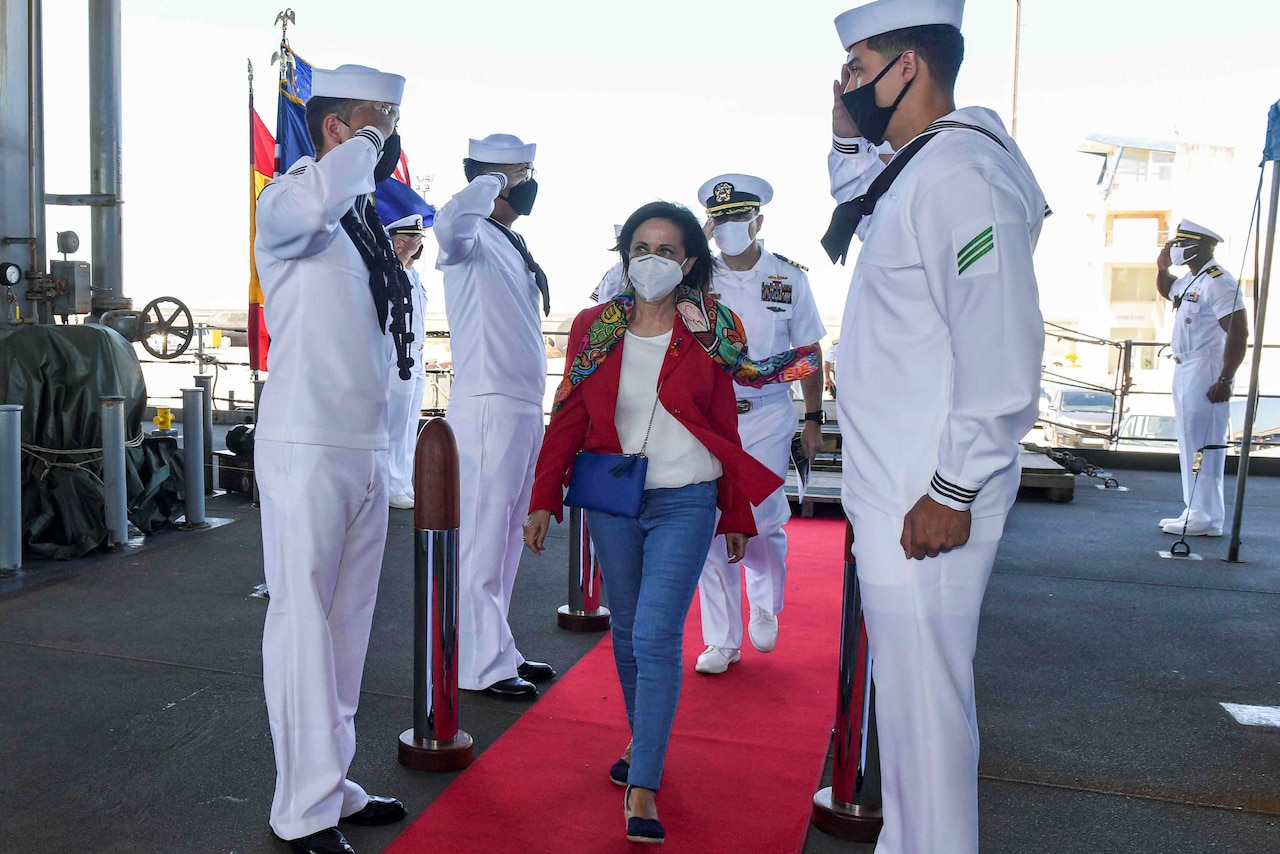 A woman in civilian clothing walks on a red carpet aboard a ship.