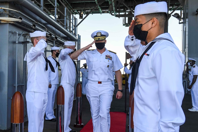 A naval officer walks on a red carpet aboard a ship.
