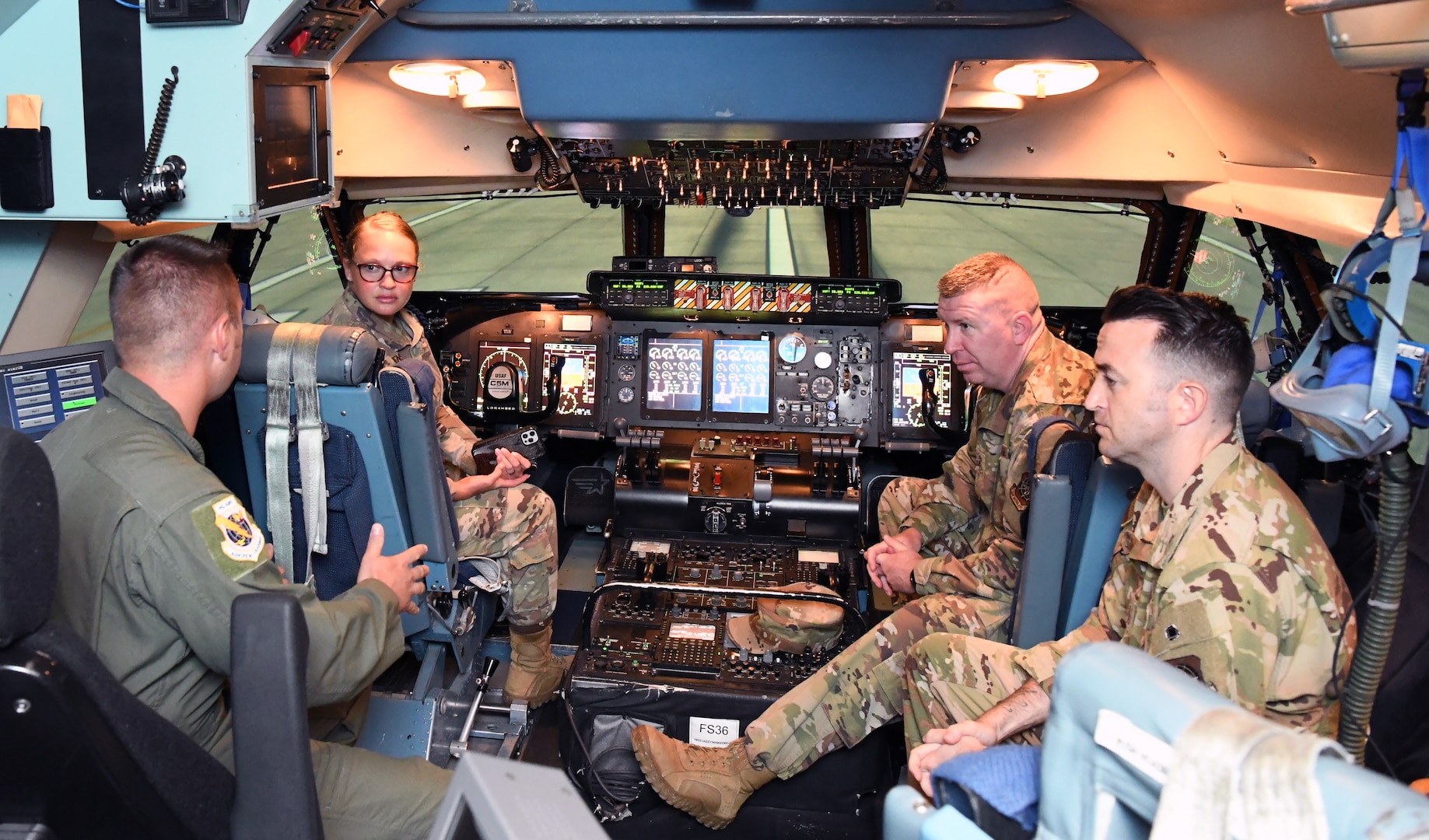 Tech. Sgt. Morgan Grebens (middle-left), 37th Training Group, and Chief Master Sgt. Chad Bickley (middle-right), 18th Air Force command chief, listen while Master Sgt. Christopher Boots (left) and Master Sgt. Erik Dunning (right), both with Air Mobility Command, describe how instructors use the C-5M Super Galaxy simulator to train pilots during a tour of the 733rd Training Squadron at Joint Base San Antonio-Lackland, Texas, July 8, 2021. As part of a multi-day tour of several JBSA units, Bickley visited with 733rd TRS leaders to discuss training challenges and strengths, see the virtual reality training equipment, cargo load trainer facility and the simulator. (U.S. Air Force photo by Master Sgt. Kristian Carter)