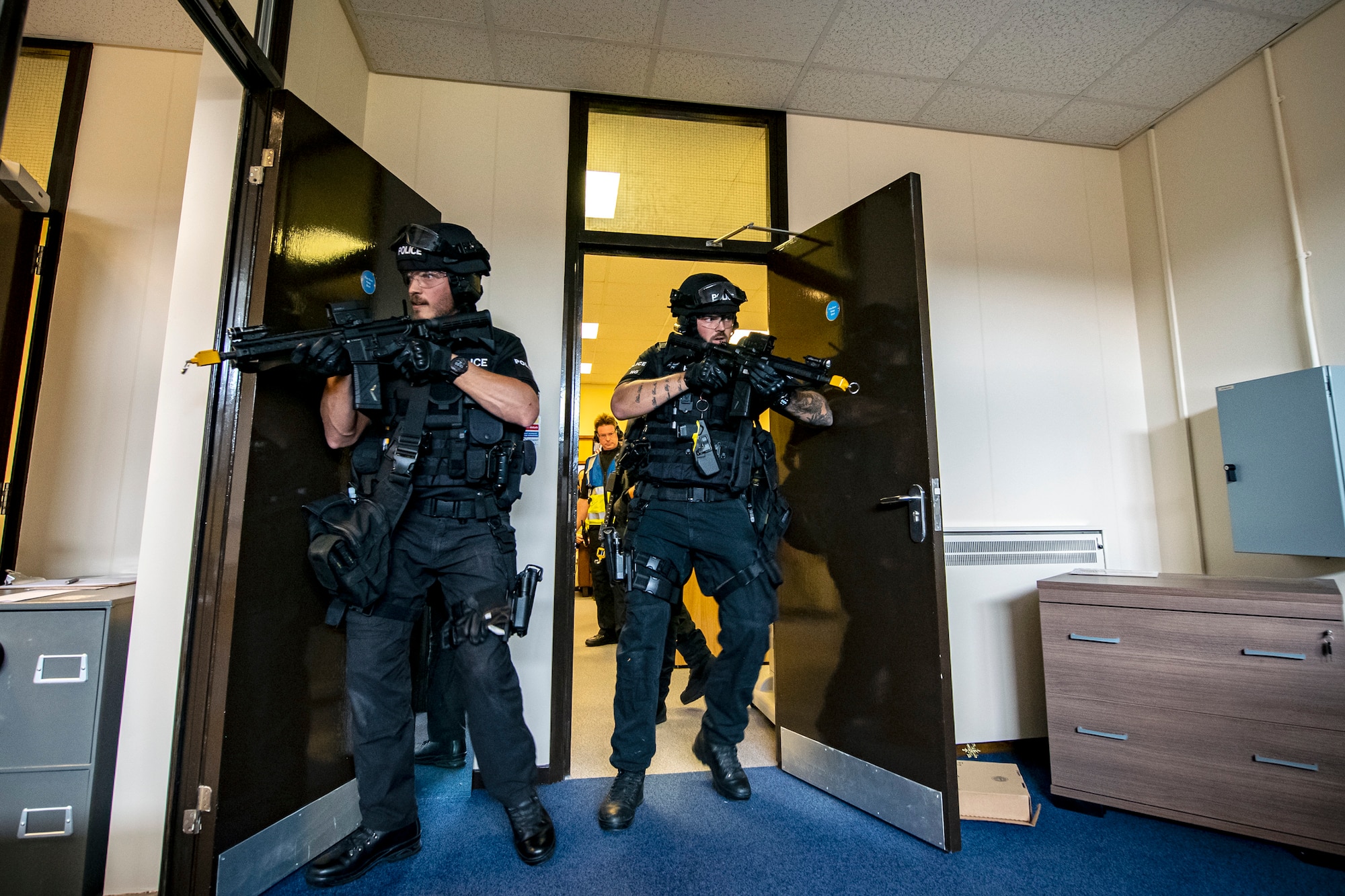 A simulated active shooter, left, engages with police officers from the Northamptonshire police department, during a tri-agency active shooter response exercise at RAF Croughton, England, June 30, 2021. Airmen from the 422nd Security Forces Squadron along with police officers from the NHPD and Ministry of Defense, participated in multiple exercises to enhance their search and seizure tactics, strengthen local ties and gain rapport with their fellow officers. (U.S. Air Force photo by Senior Airman Eugene Oliver)