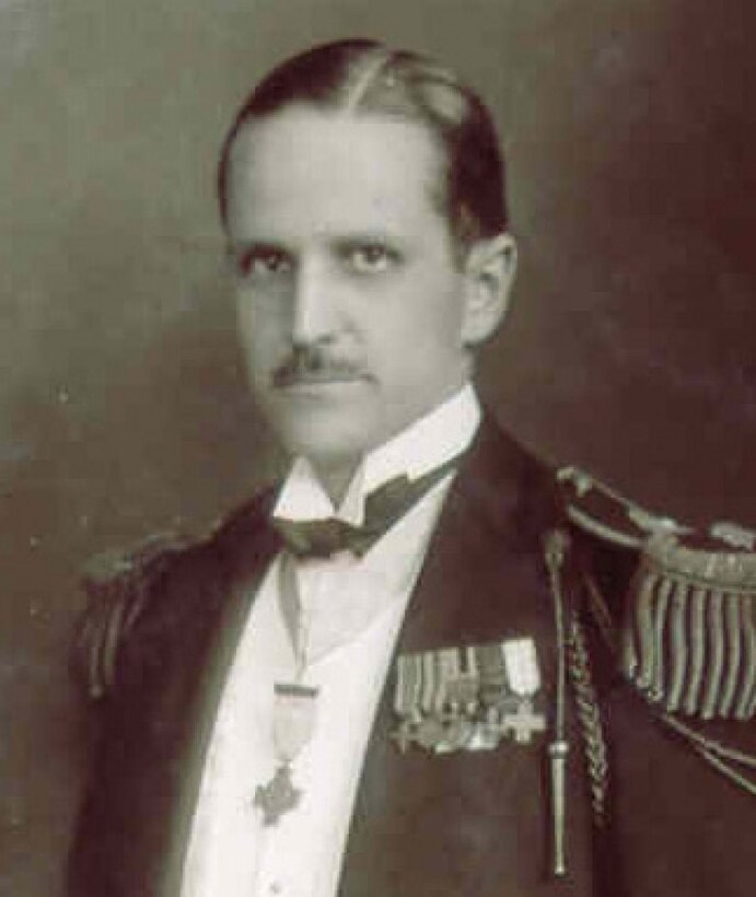 A man wearing a jacket, epaulettes and a medal around his neck poses for a photo.