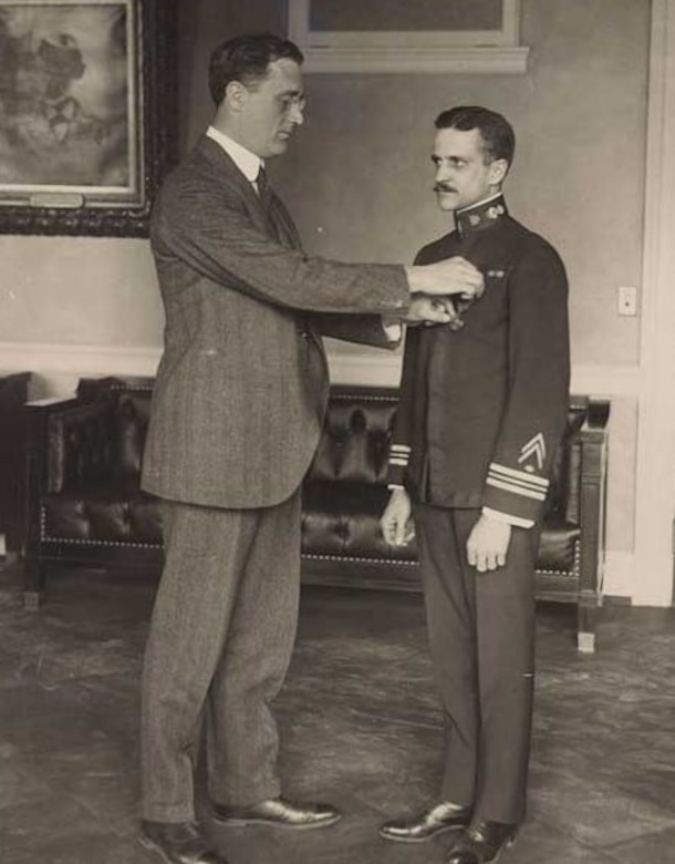 A tall man pins a medal to another man's chest lapel.