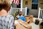 Photo of woman and child carrying boxes into a home.