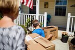 Photo of woman and child carrying boxes into a home.