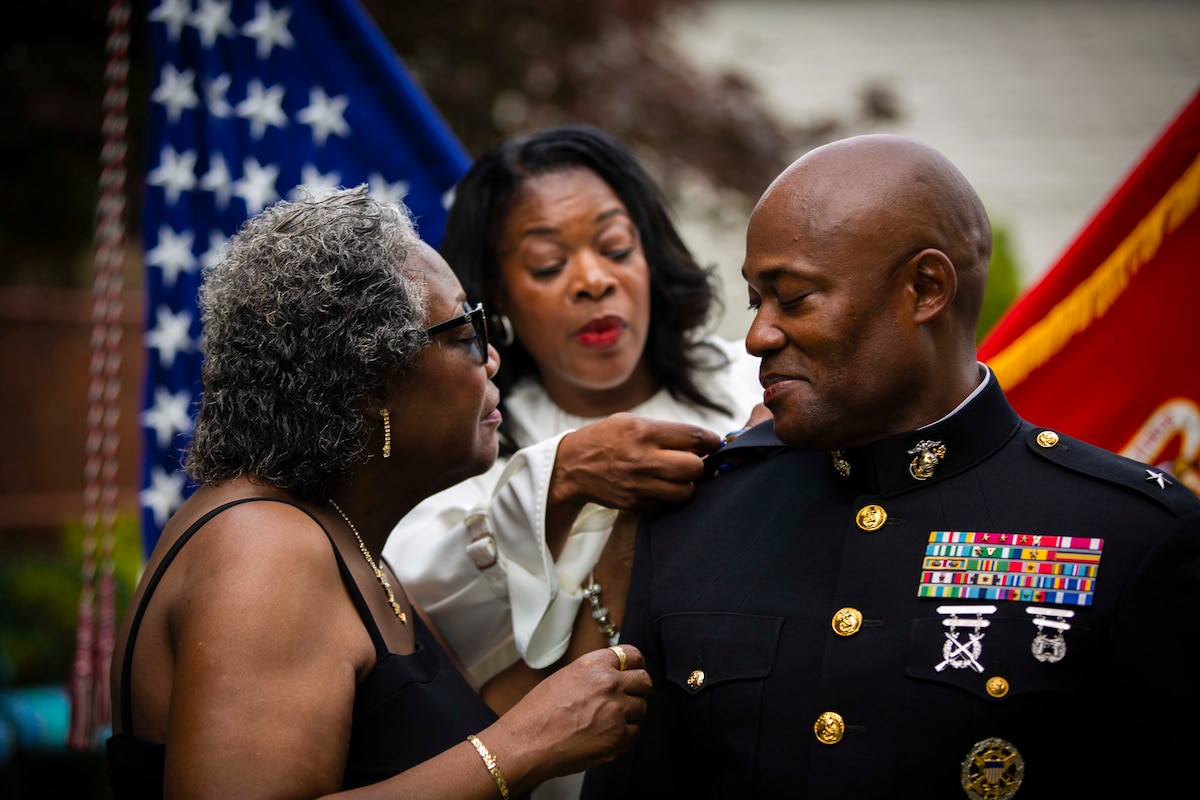 Two women place a pin onto a Marine's uniform.