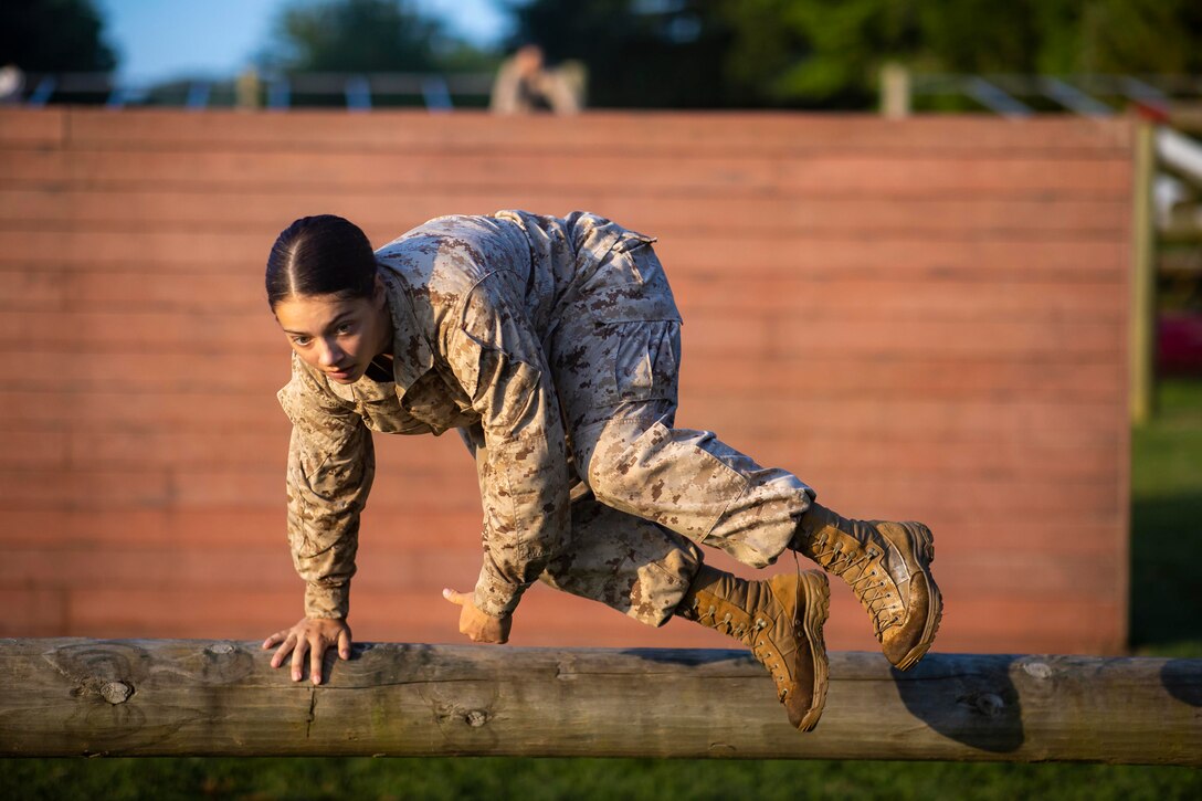 A Marine jumps over a wooden log.