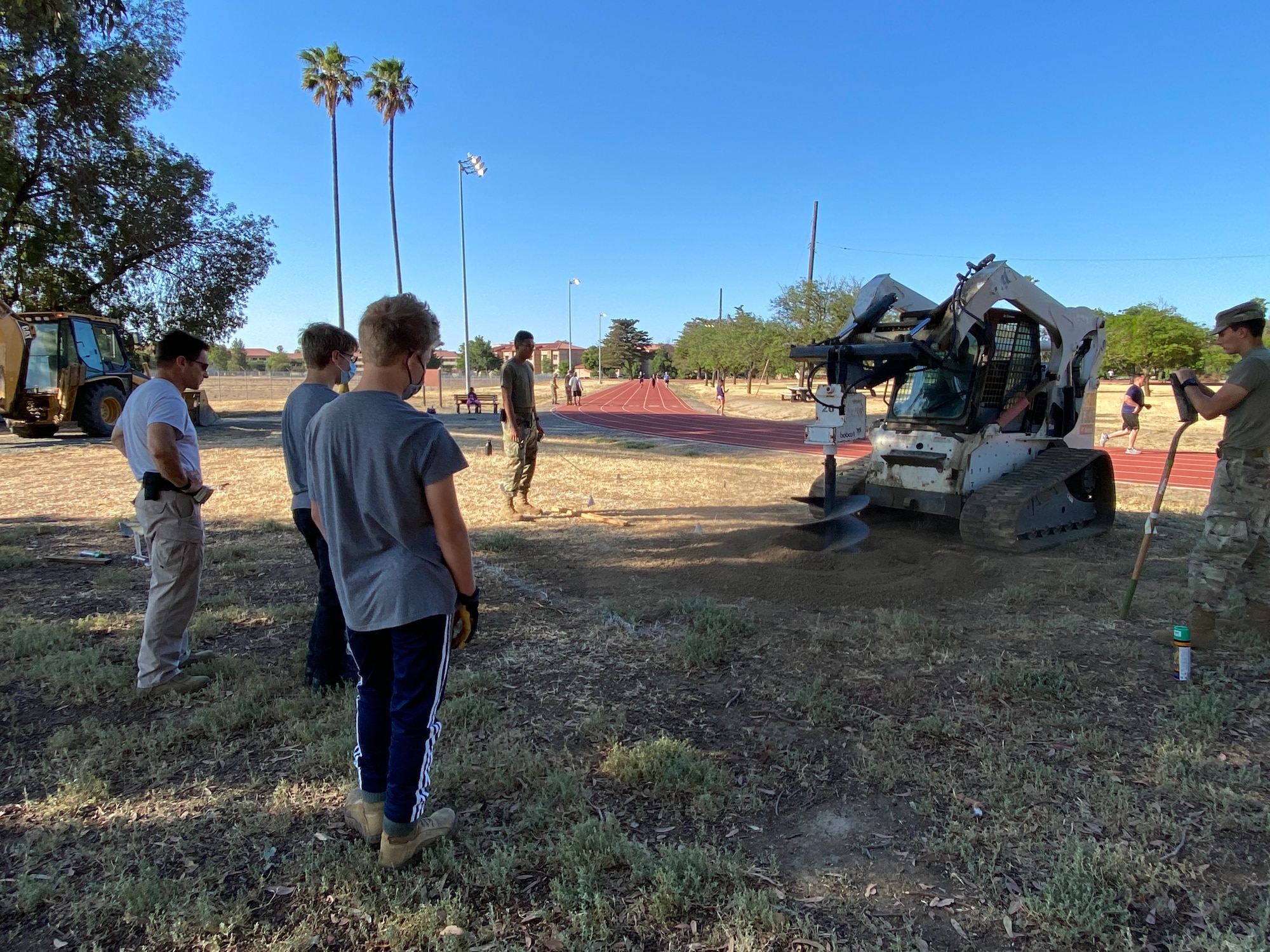 Boy scouts and Airmen work together to install pull-up bars on a dirt patch.