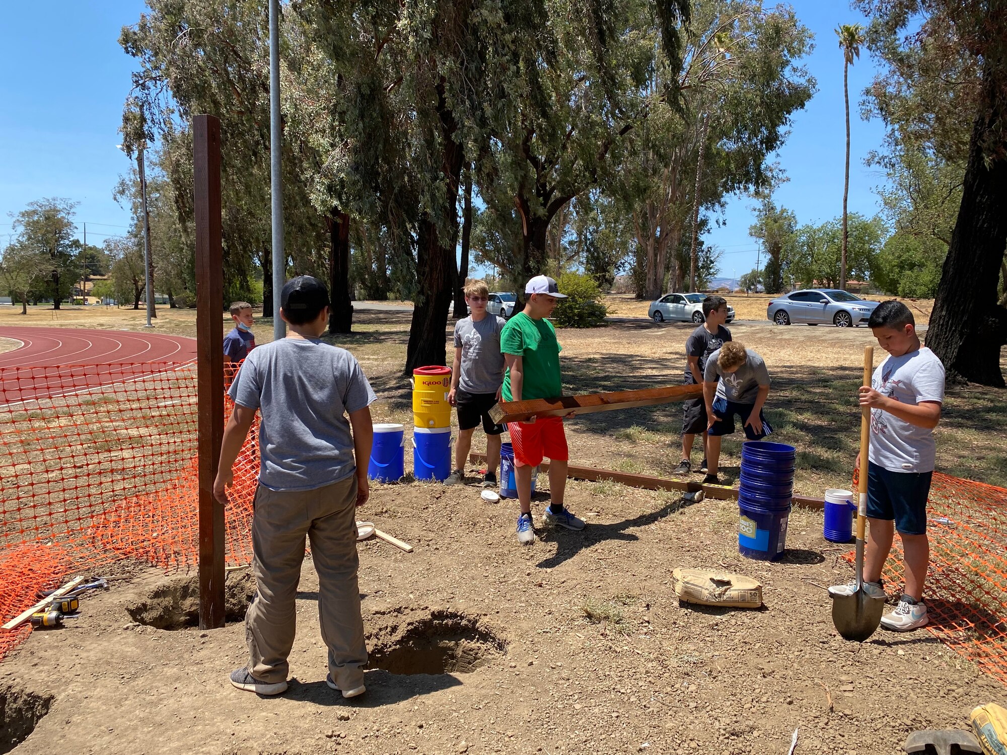 Boy scouts and Airmen work together to install pull-up bars on a dirt patch.