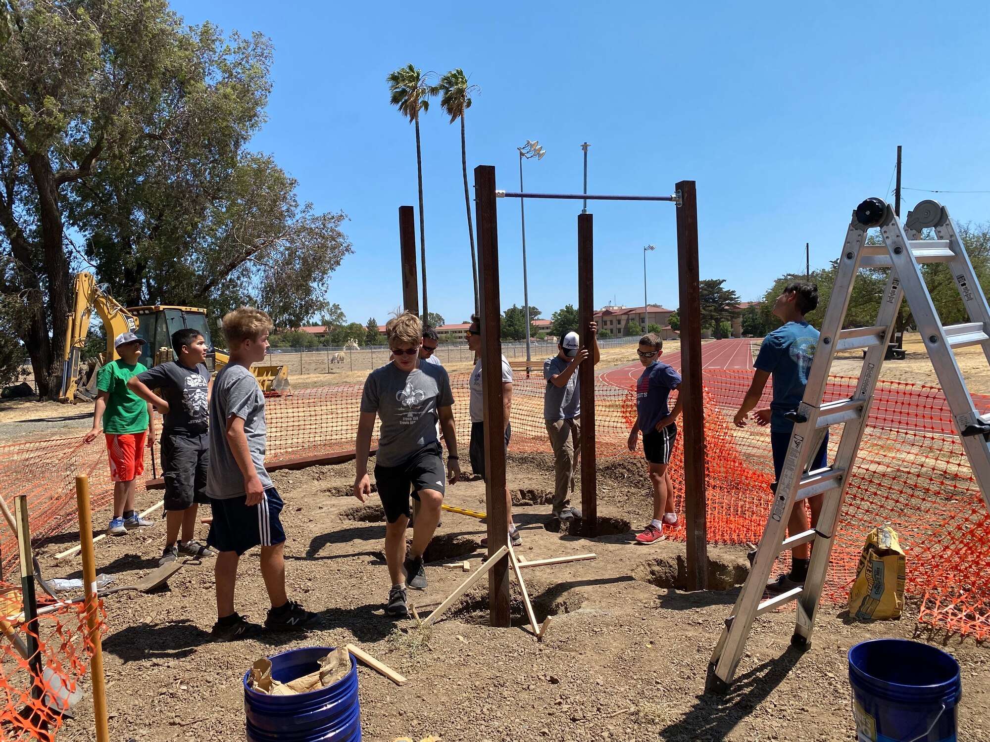 Boy scouts and Airmen work together to install pull-up bars on a dirt patch.