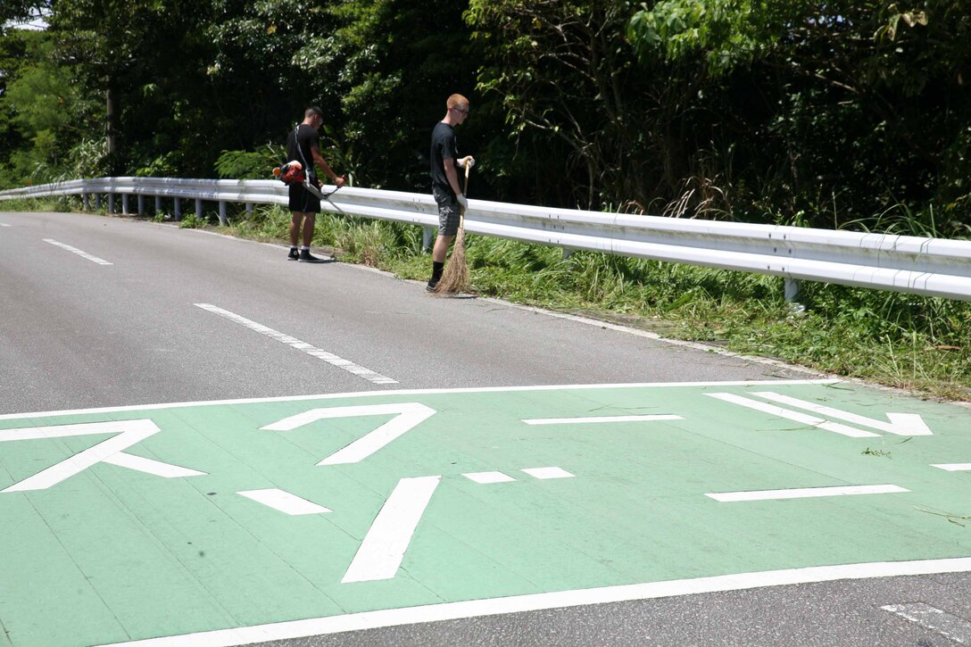 気温３５度近くの炎天下の下、ボランティアで草刈り作業に励む隊員ら、沖縄県金武町中川地区公民館近く、2021年7月14日