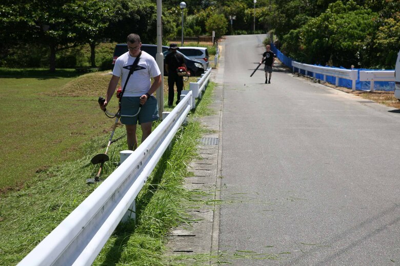 気温３５度近くの炎天下の下、ボランティアで草刈り作業に励む隊員ら、沖縄県金武町中川地区公民館近く、2021年7月14日