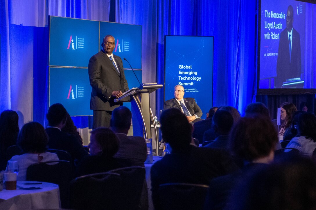 A man stands on a stage and speaks at a podium in front of a room of people.