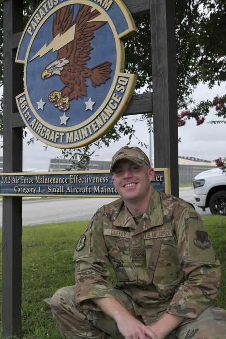 Photo shows Airman squatting in front of his unit's sign that says 461st Aircraft Maintenance Squadron.