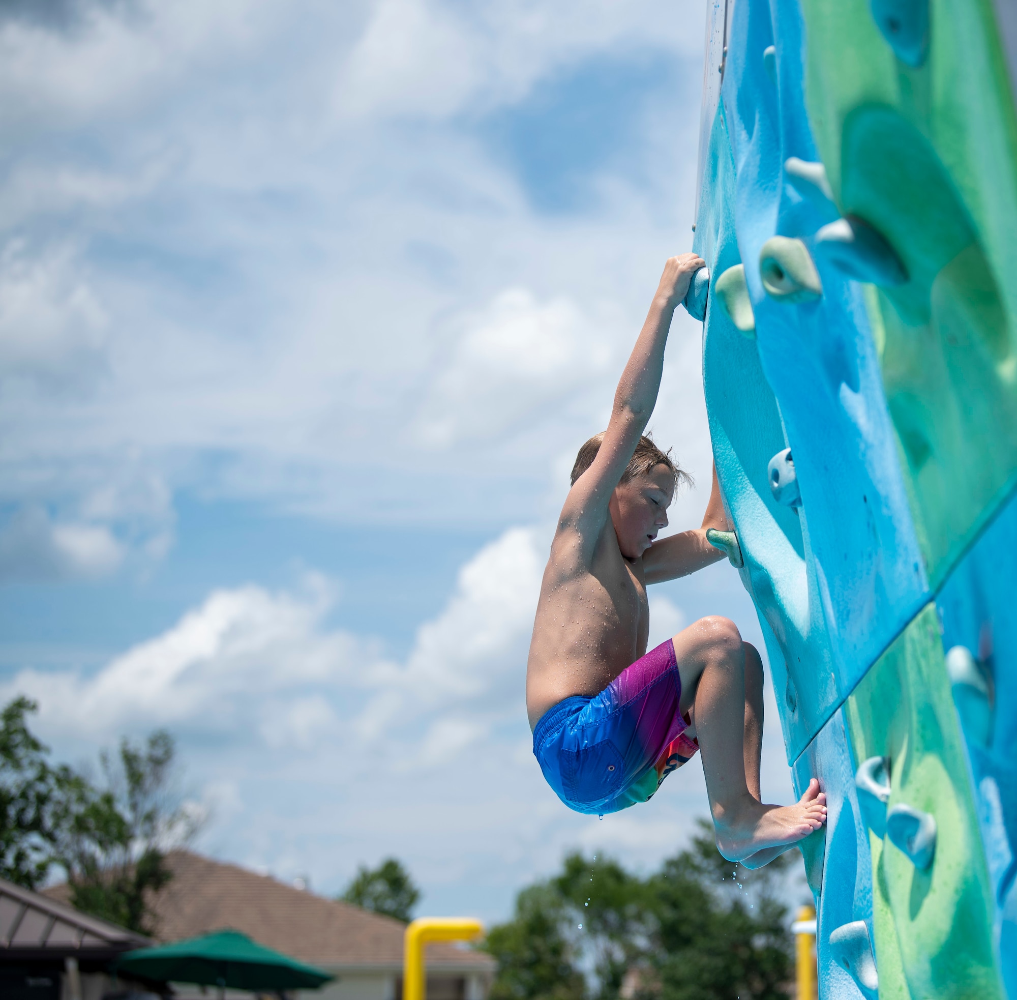 A boy climbs a rock wall at the Oasis Pool at Dover Air Force Base, Del., July 14, 2021. During summer break, the pool is open 11 am to 7 pm daily for military members, family and friends. The pool no longer has block sessions for attendees, but has a capacity limit of 200 people.  (U.S. Air Force photo by Tech. Sgt. Nicole Leidholm)