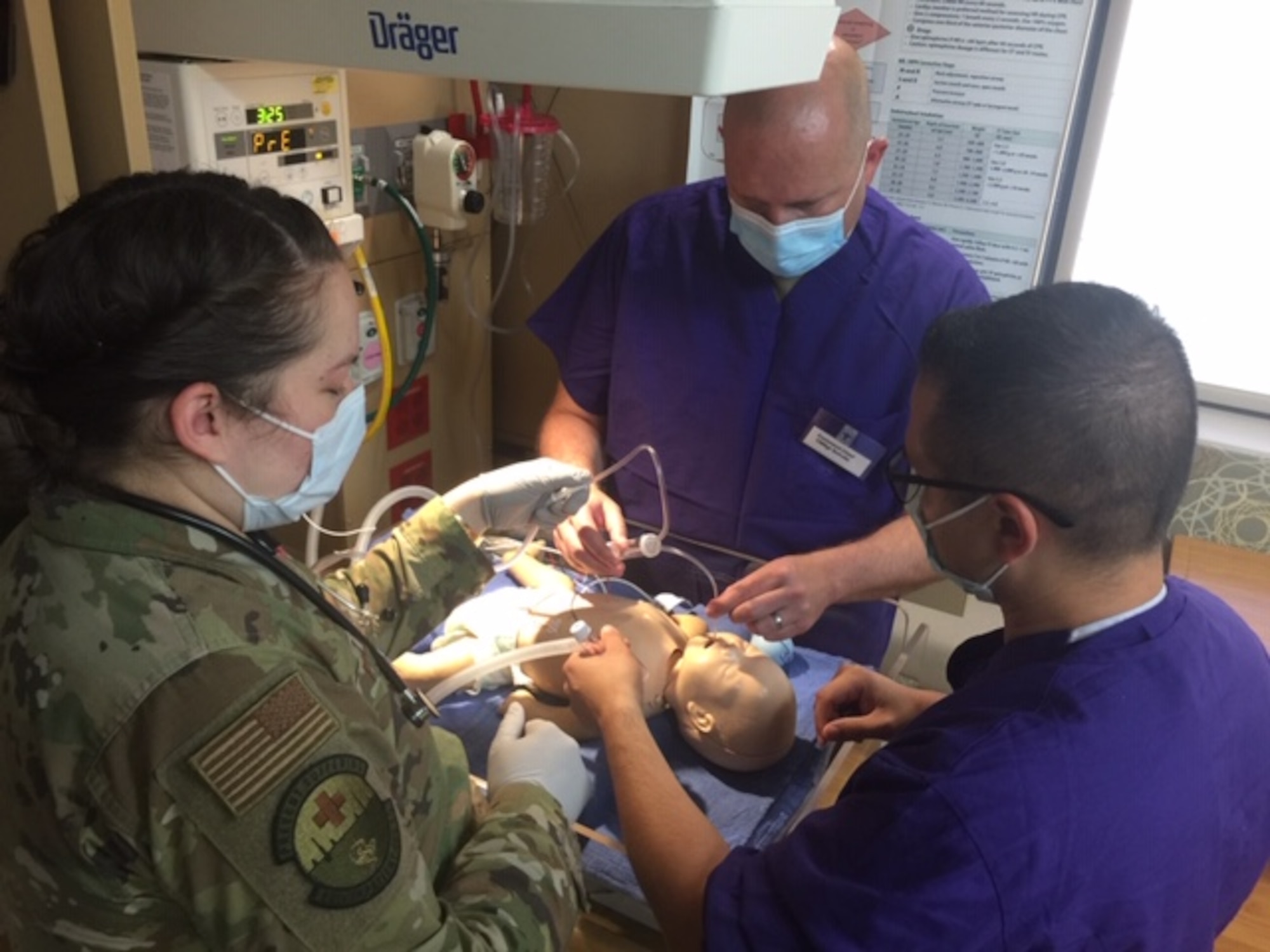 Three airman treat an infant mannequin in a hospital