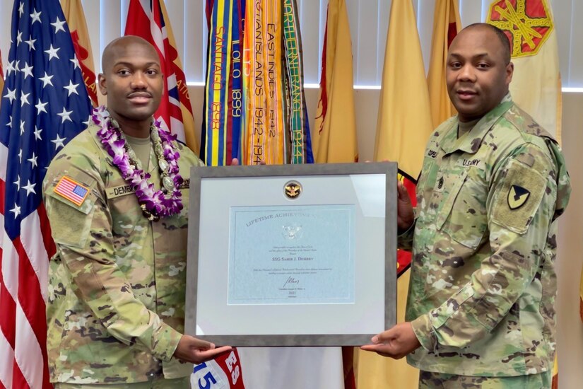 Two soldiers stand for a photo and hold up a plaque.