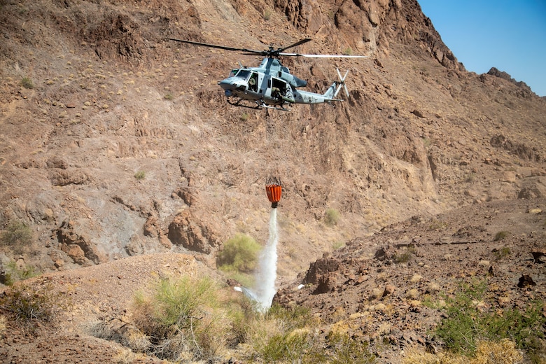 A U.S. Marine Corps UH-1Y Venom with Marine Operational Test and Evaluation Squadron (VMX) 1, dumps water into a watering hole near the Chocolate Mountain Aerial Gunnery Range, Calif., July 7, 2021. Man-made watering holes help animals in the desert access water easily all year round. (U.S. Marine Corps photo by Lance Cpl Gabrielle Sanders)