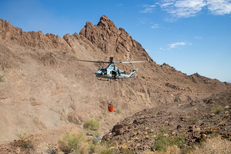 A U.S. Marine Corps UH-1Y Venom with Marine Operational Test and Evaluation Squadron (VMX) 1, dumps water into a watering hole near the Chocolate Mountain Aerial Gunnery Range, Calif., July 7, 2021. Man-made watering holes help animals in the desert access water easily all year round. (U.S. Marine Corps photo by Lance Cpl Gabrielle Sanders)