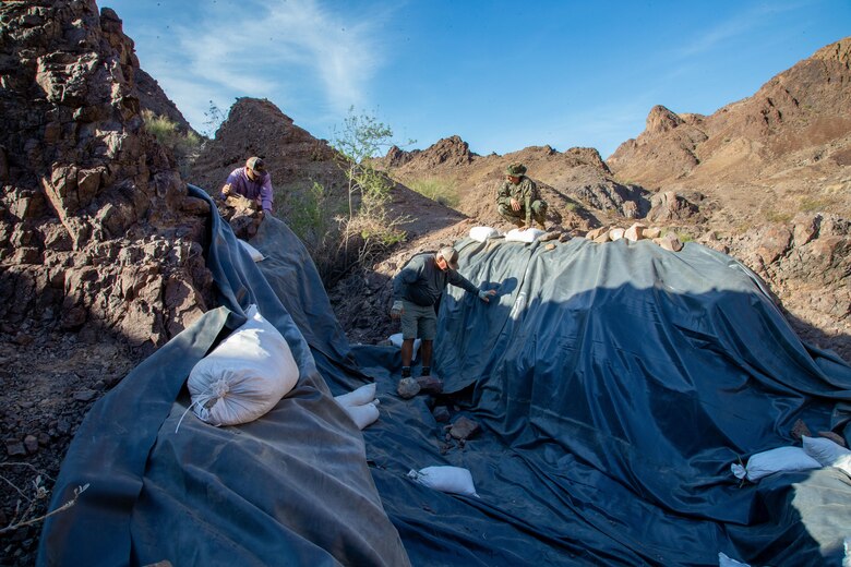 U.S. Marine Corps Sergeant Austin Hall, an aviation radar technician with Marine Operational Test and Evaluation Squadron (VMX) 1, lays tarp down in preparation for the watering hole to collect water near the Chocolate Mountain Aerial Gunnery Range, Calif., July 7, 2021. Man-made watering holes help animals in the desert access water easily all year round. (U.S. Marine Corps photo by Lance Cpl Gabrielle Sanders)