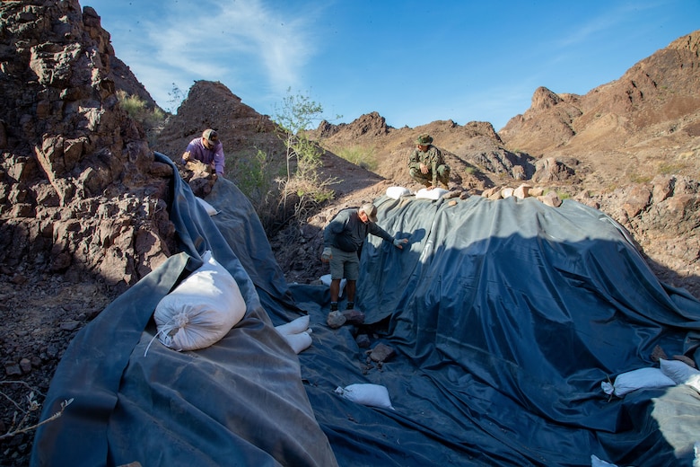 U.S. Marine Corps Sergeant Austin Hall, an aviation radar technician with Marine Operational Test and Evaluation Squadron (VMX) 1, lays tarp down in preparation for the watering hole to collect water near the Chocolate Mountain Aerial Gunnery Range, Calif., July 7, 2021. Man-made watering holes help animals in the desert access water easily all year round. (U.S. Marine Corps photo by Lance Cpl Gabrielle Sanders)