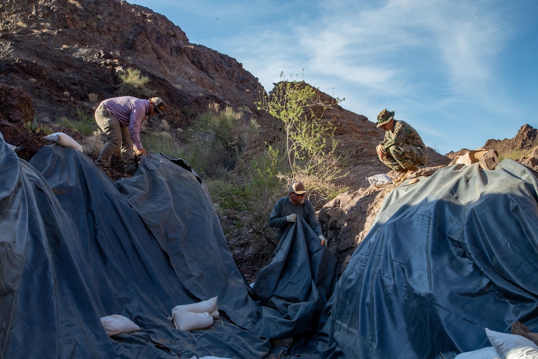 U.S. Marine Corps Sgt. Austin Hall, an aviation radar technician with Marine Operational Test and Evaluation Squadron (VMX) 1, lays tarp down in preparation for the watering hole to collect water near the Chocolate Mountain Aerial Gunnery Range, Calif., July 7, 2021. Man-made watering holes help animals in the desert access water easily all year round. (U.S. Marine Corps photo by Lance Cpl Gabrielle Sanders)