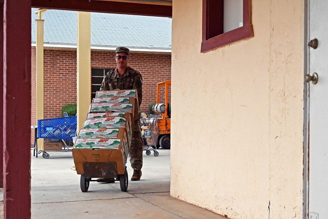 A guardsman pushes a dolly with boxes of donated food.