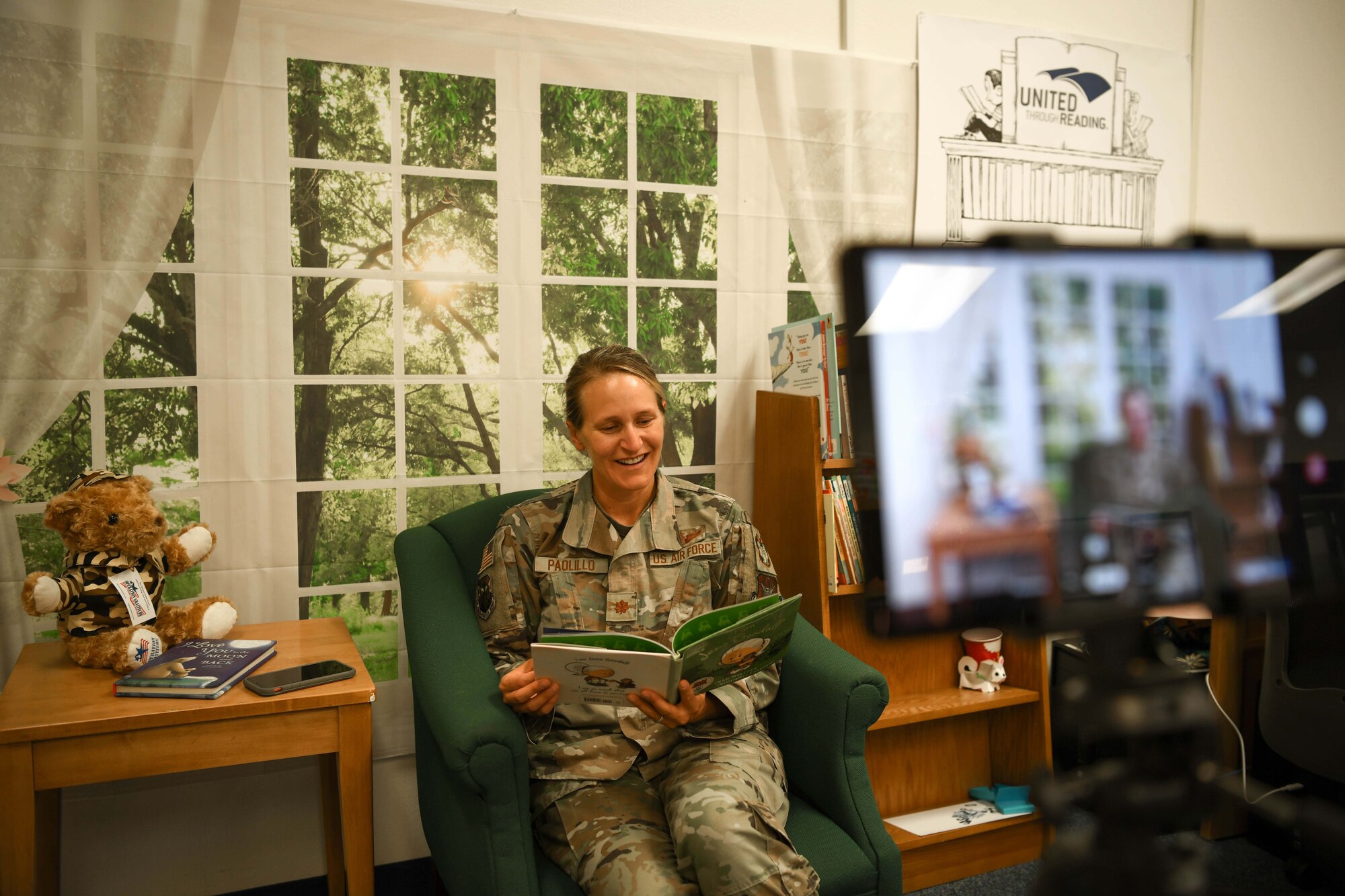Reserve Citizen Airman Maj. Katherine Paolillo, 944th Fighter Wing inspector general, reads a book to her child using the United Through Reading app at the 56th Fighter Wing Base Library on Luke Air Force Base, Arizona, June 17, 2021. The 944th Fighter Wing Airman and Family Readiness Center and the base library teamed up to provide anyone with access to the base a place to stop by and read a book to a loved one. The non-profit program will send the recording to an email address designated by the member and also provide the book to the military family for free.