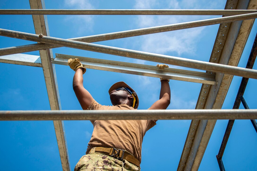 A sailor grabs onto metal scaffolding.