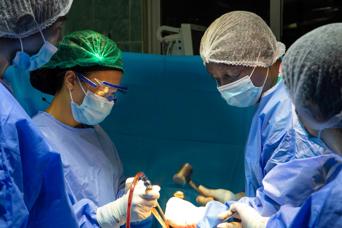 Four people wearing medical gear perform a surgery.