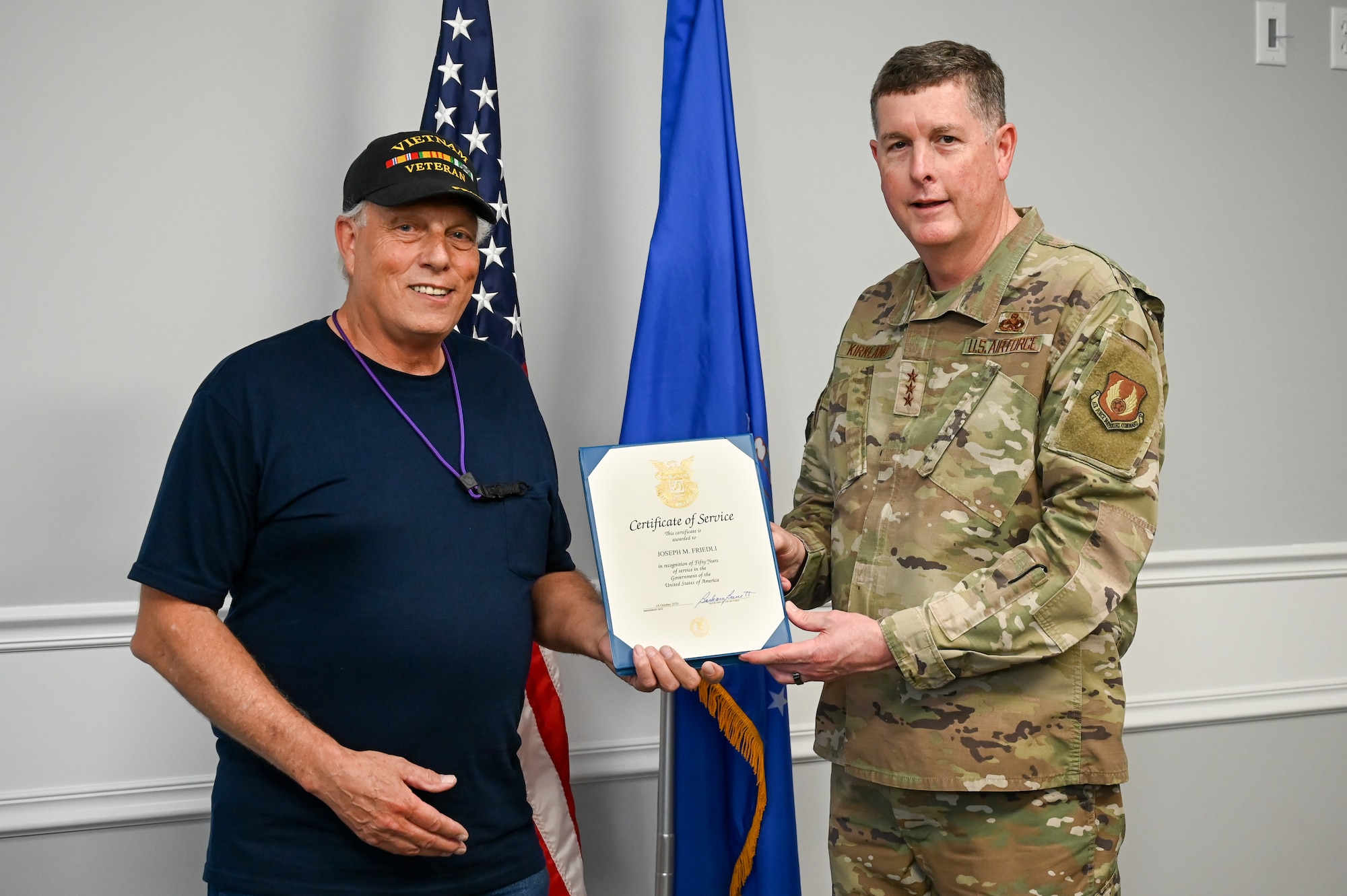 Joseph Friedli and Lt. Gen. Kirland pose for a photo while holding the 50-year certificate in between them.