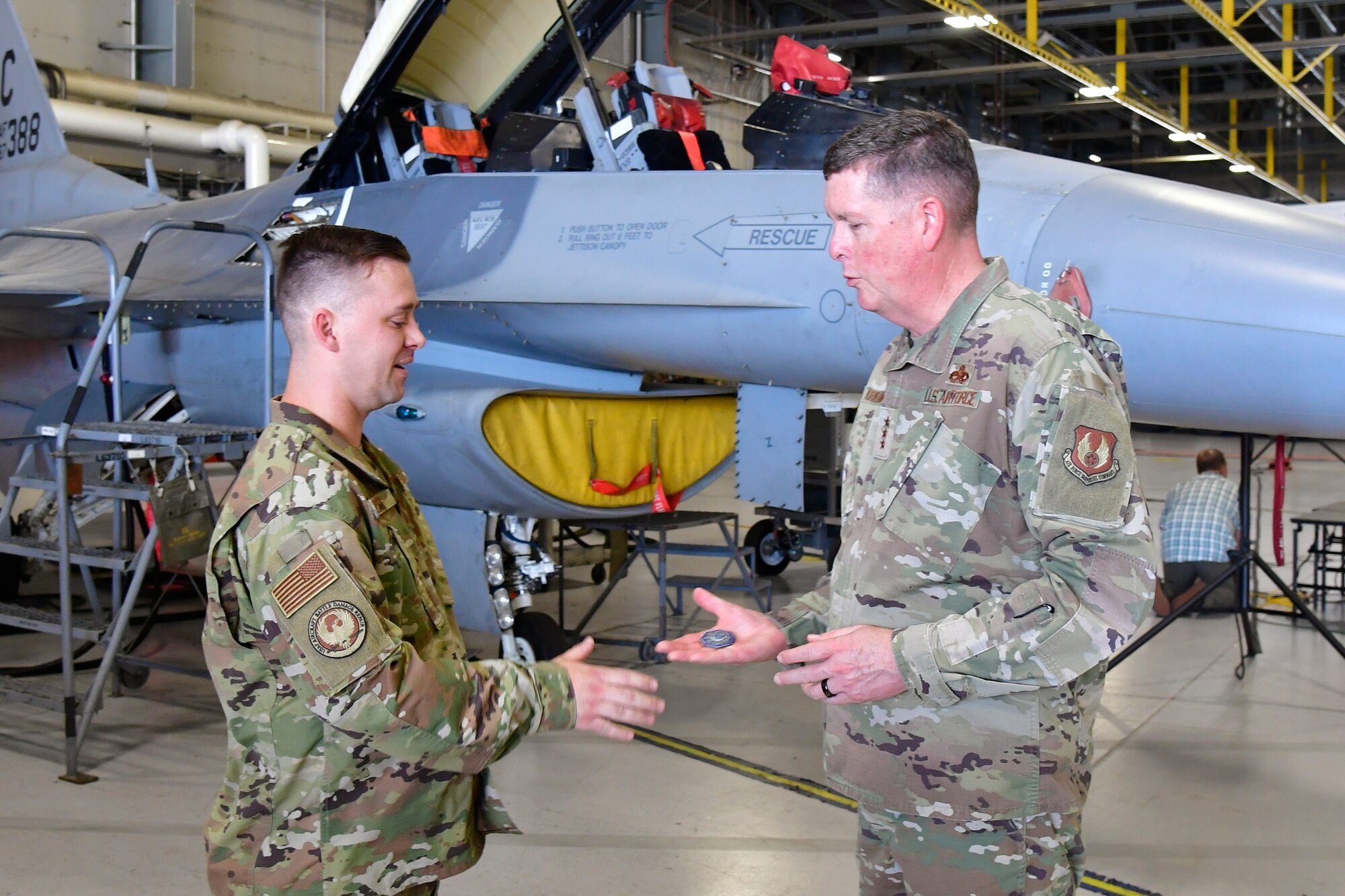 Tech. Sgt. Dominic Dizes holds his hand out to Lt. Gen. Kirkland who is holding a commander's coin in his palm.