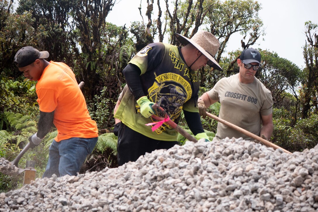 Three airmen shovel gravel.