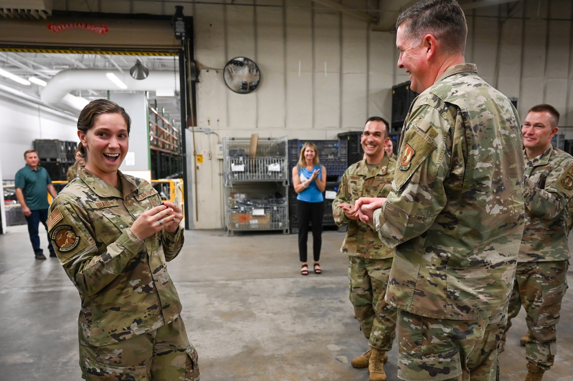 Airman 1st Class Braud stands in surprise in front of a smiling Lt. Gen. Kirkland and other Airmen in the background.