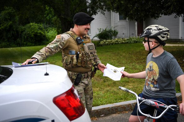 Senior Airman Carlos Howard, 66th Security Forces Squadron Positive Policing program lead, presents a Blue Bucks certificate to Parker Jones, Hanscom resident, for wearing a helmet while riding a bike at Hanscom Air Force Base, Mass., July 13. The Positive Policing program allows 66 SFS defenders to recognize community members for adhering to safety protocols or traffic laws. (U.S. Air Force photo by Lauren Russell)