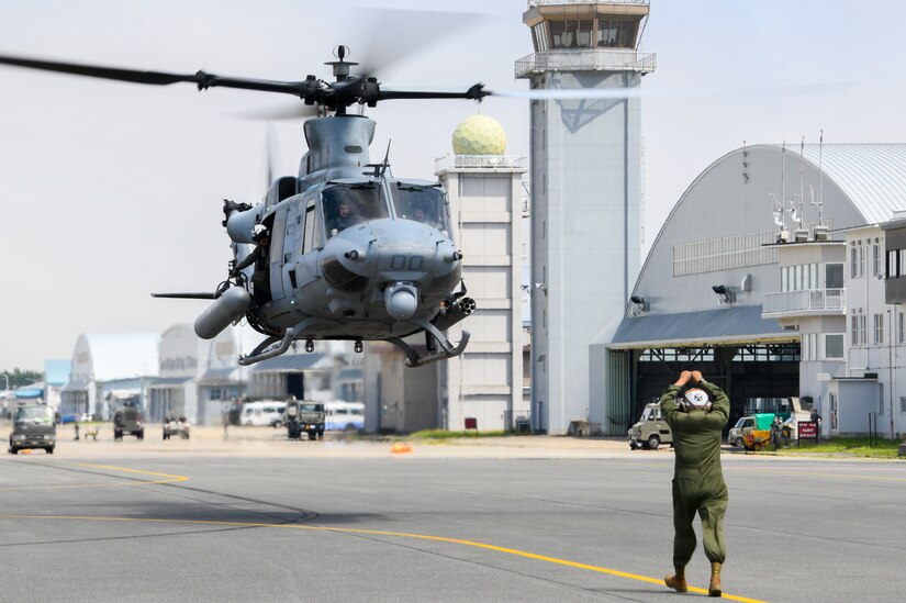 A service member signals to a helicopter as it prepares to land.