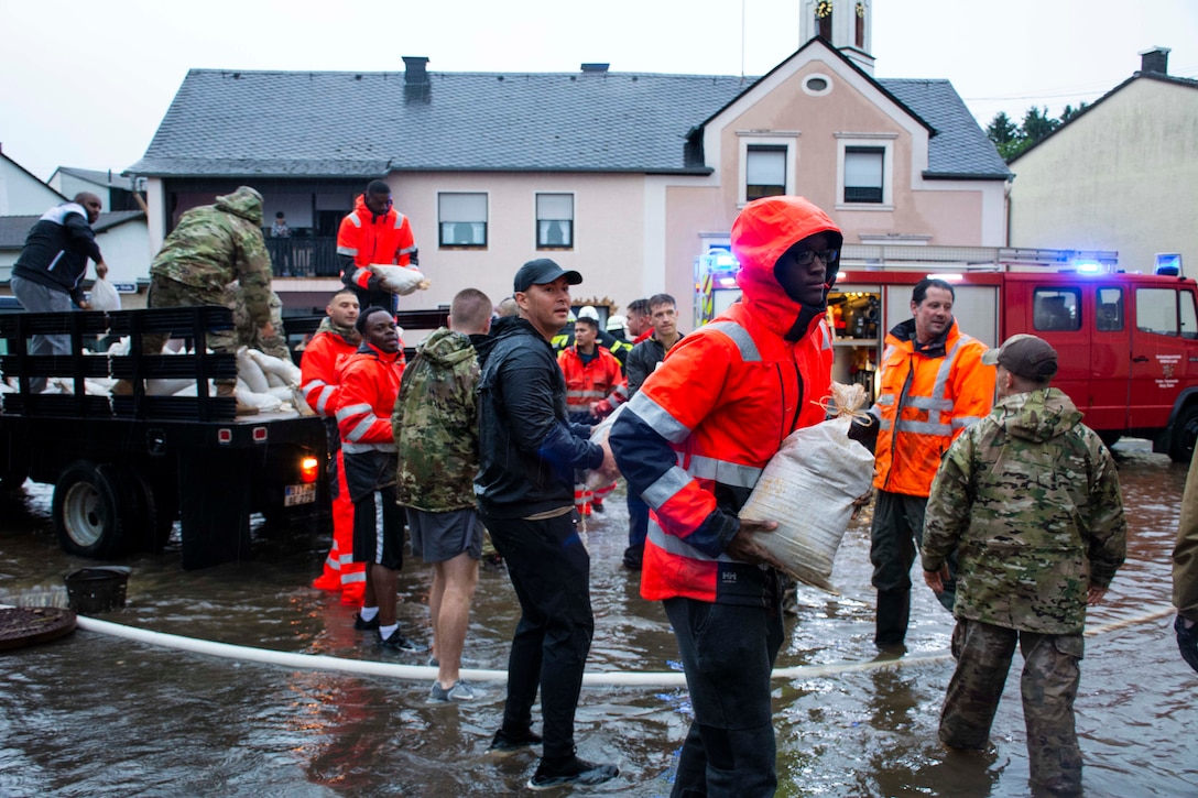 A group of airmen hand off sandbags from a truck on a flooded street.