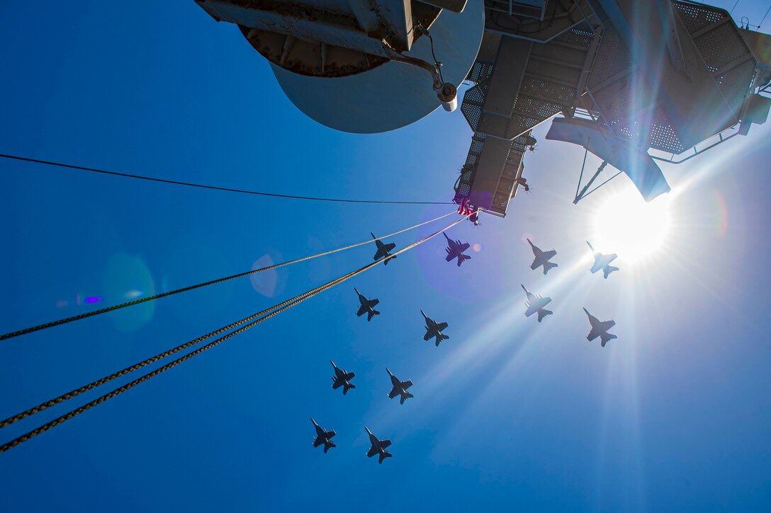 Navy jets fly in formation above a ship.