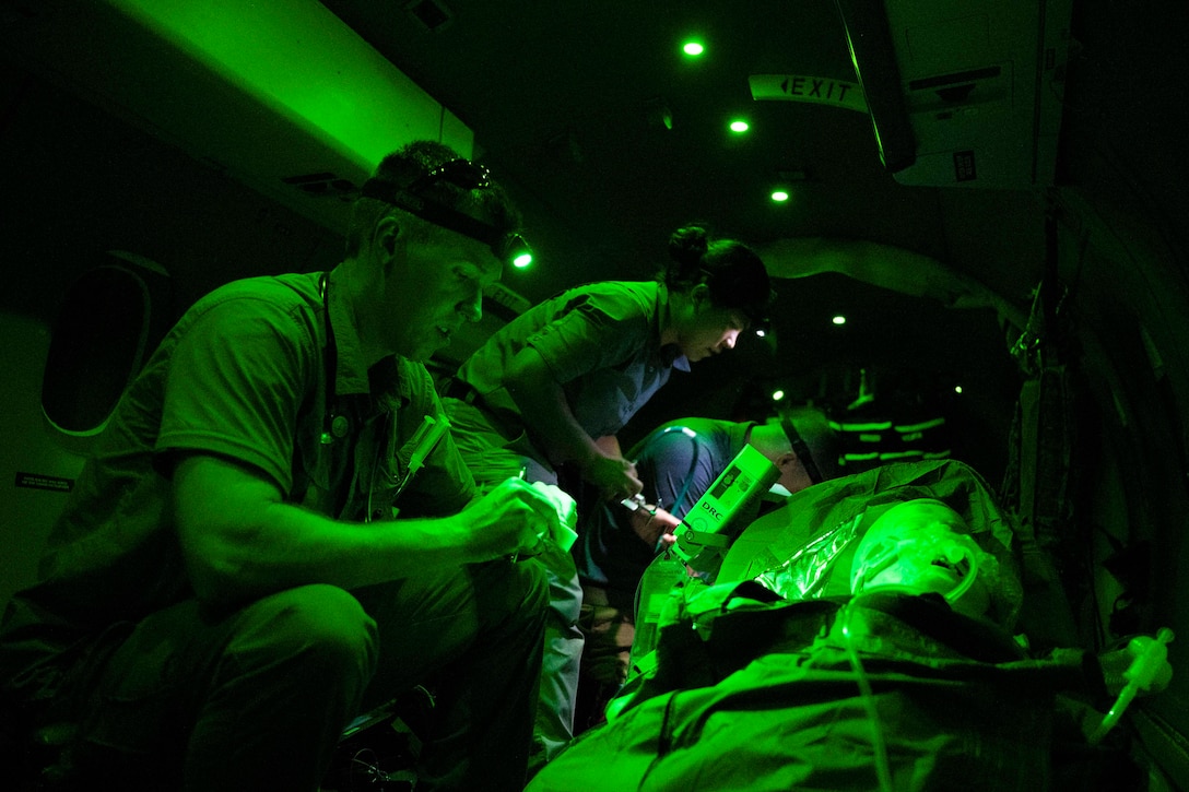 Airmen  illuminated by green light work on a dummy patient.