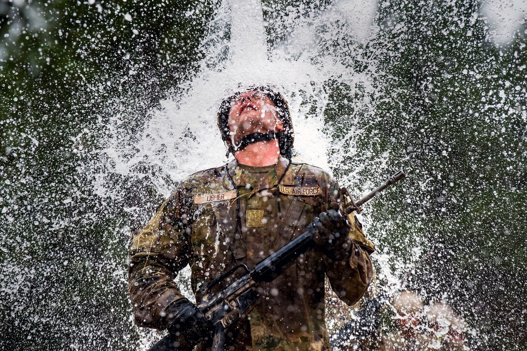 Water pours over an Air Force cadet holding a weapon, with head tilted up.