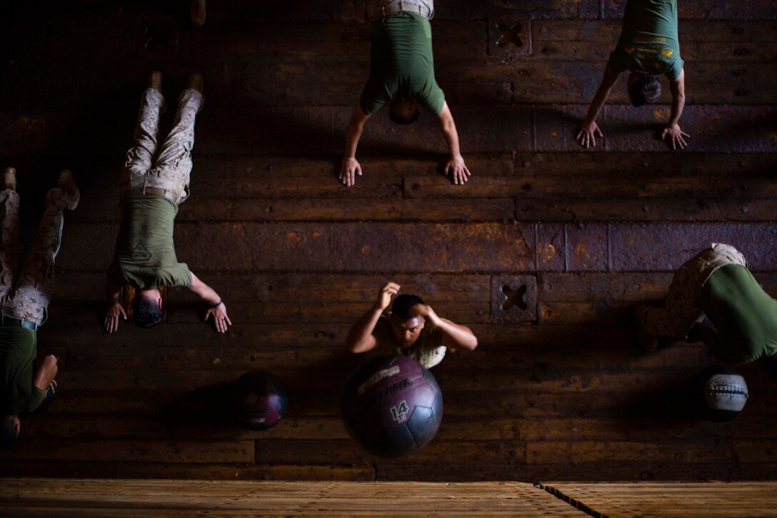 A Marine throws a ball up as other Marines assume plank positions.